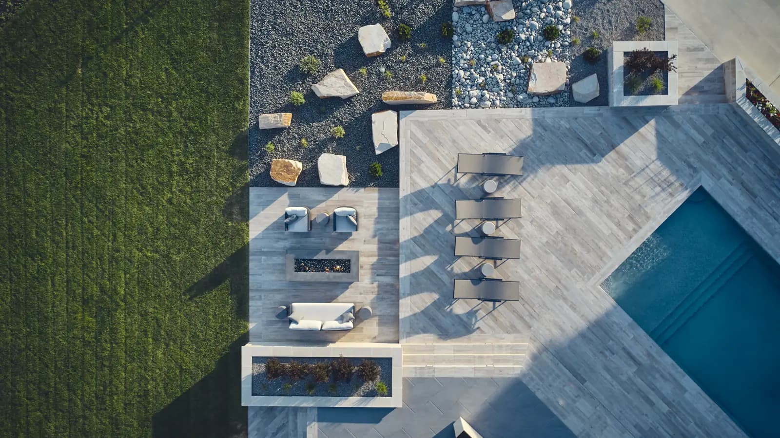 Aerial of a pool deck with chaise lounges, planters, fire lounge, and adjoining lawn
