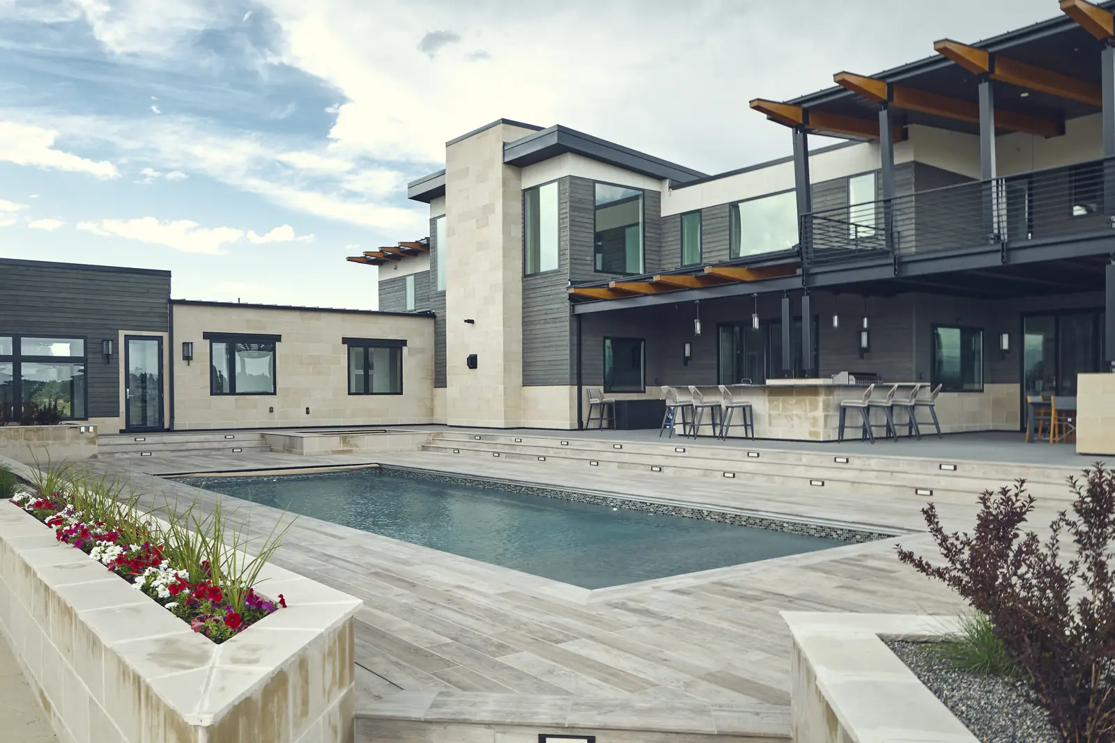 Daytime pool with raised flower planter, porcelain deck, and outdoor kitchen beyond