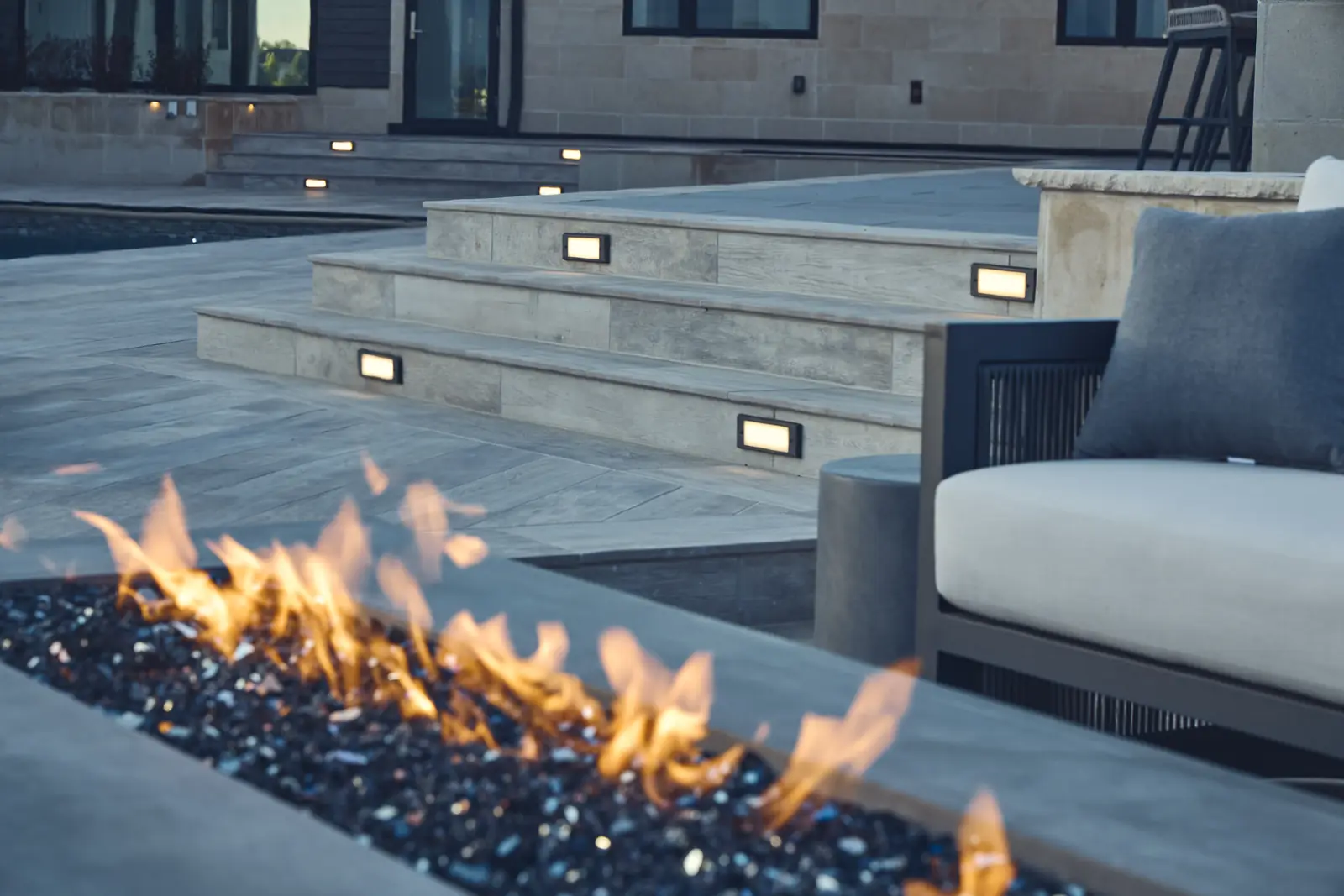 Close-up of fire glass flames with an outdoor sofa and limestone steps behind, Colorado