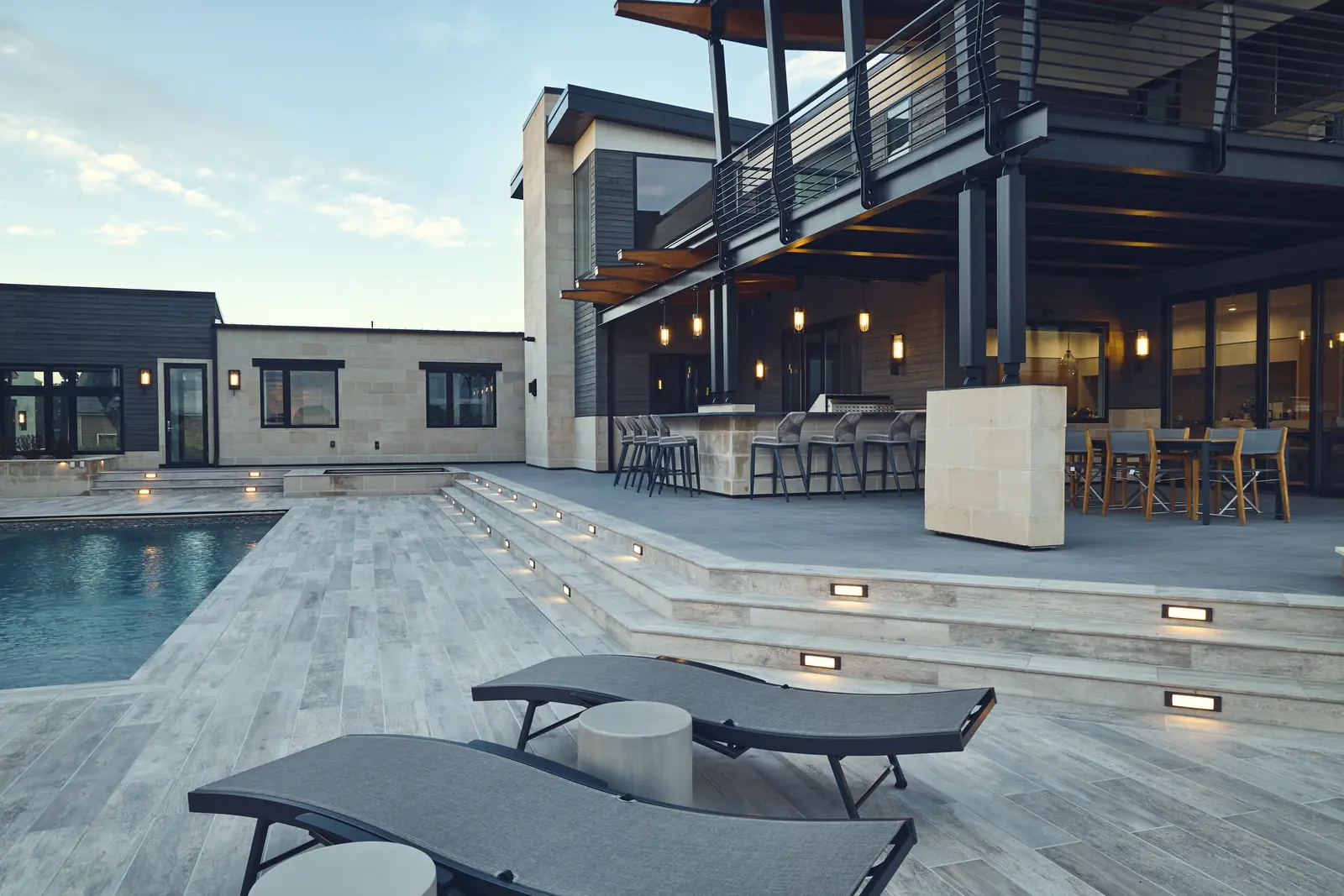Dusk view of pool steps, chaise lounges, and the balcony of a modern Colorado home