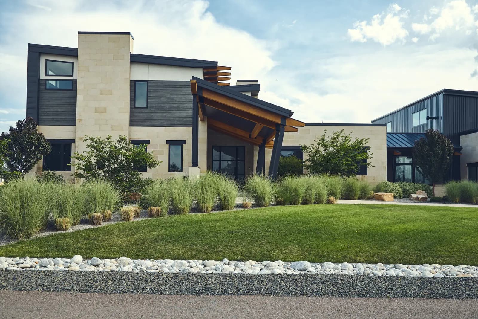 Modern stone and metal home facade with crisp lawn panels bordered by rock beds, Johnson Estate, Colorado