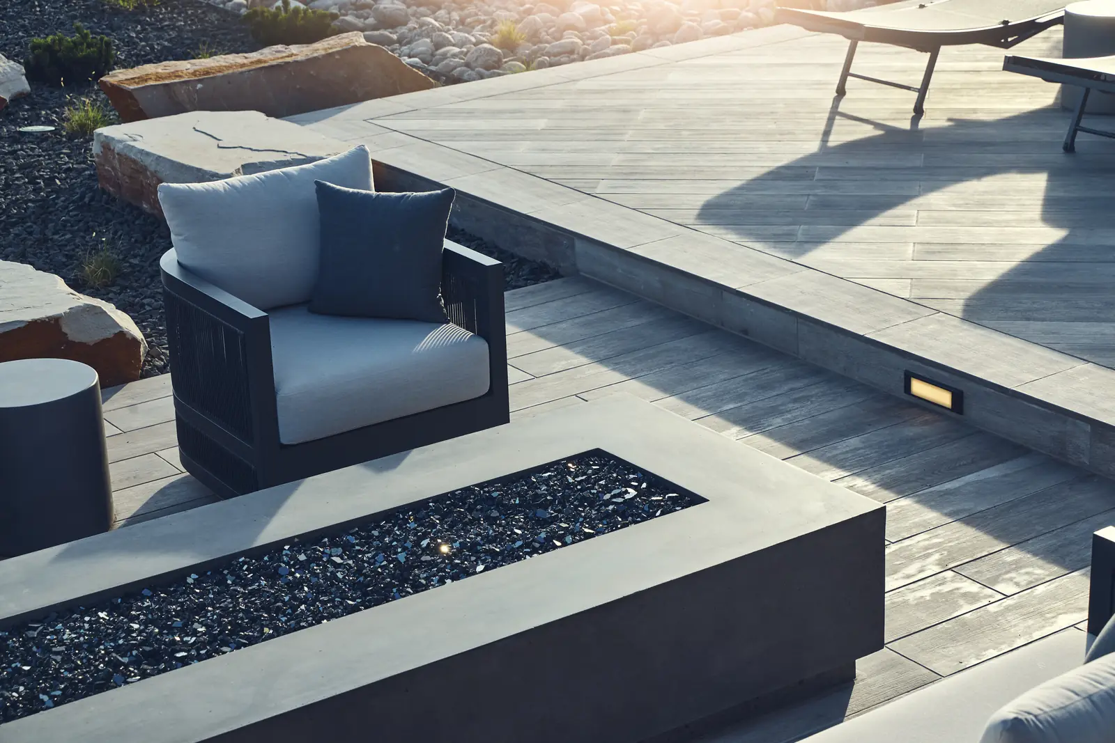 Outdoor armchair beside a linear concrete fire pit filled with black fire glass, Colorado