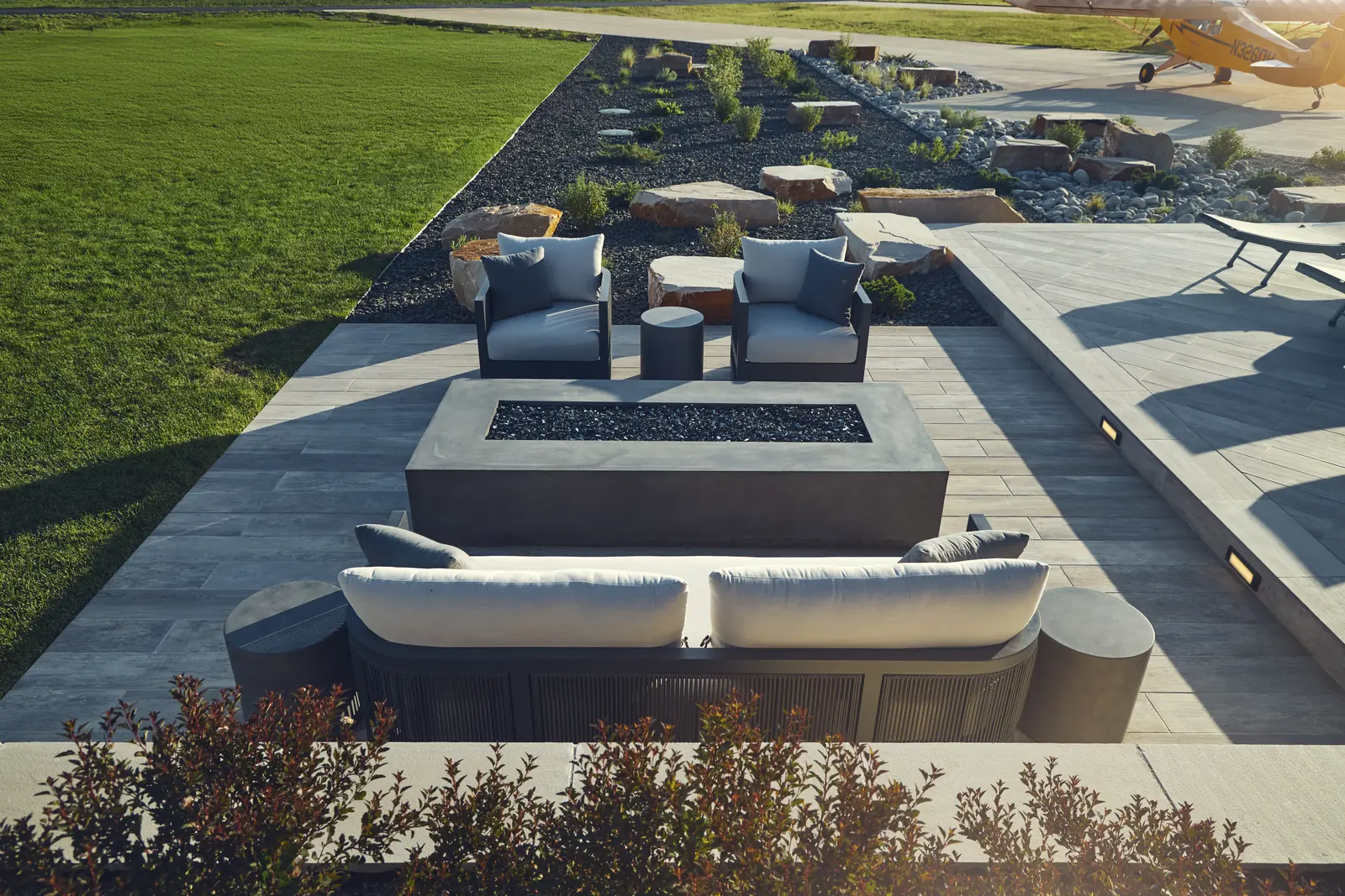 Sunken lounge with outdoor sofas around a concrete fire table at the lawn edge