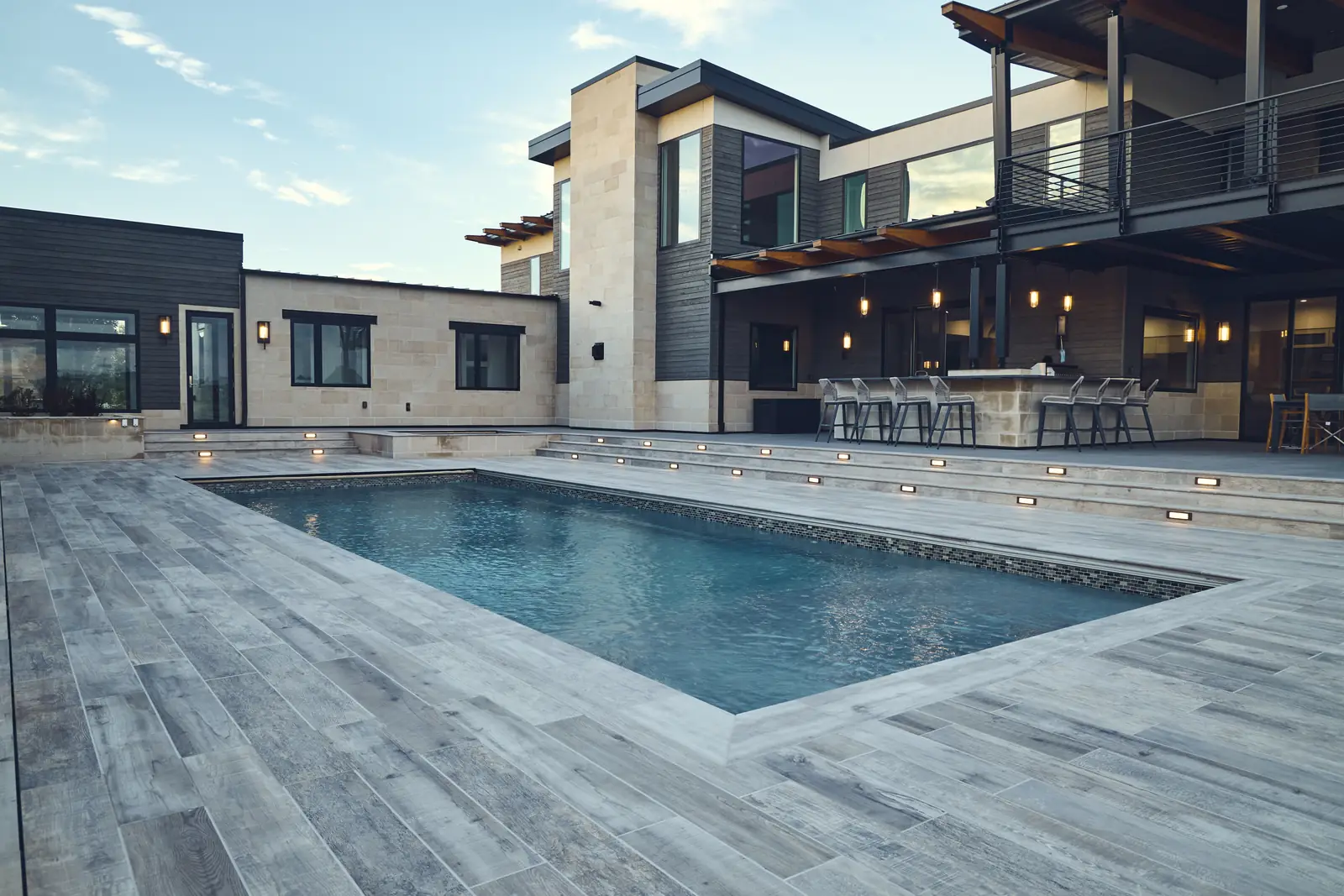 Wide view of a custom pool, modern home, and pergola-covered outdoor bar, Colorado