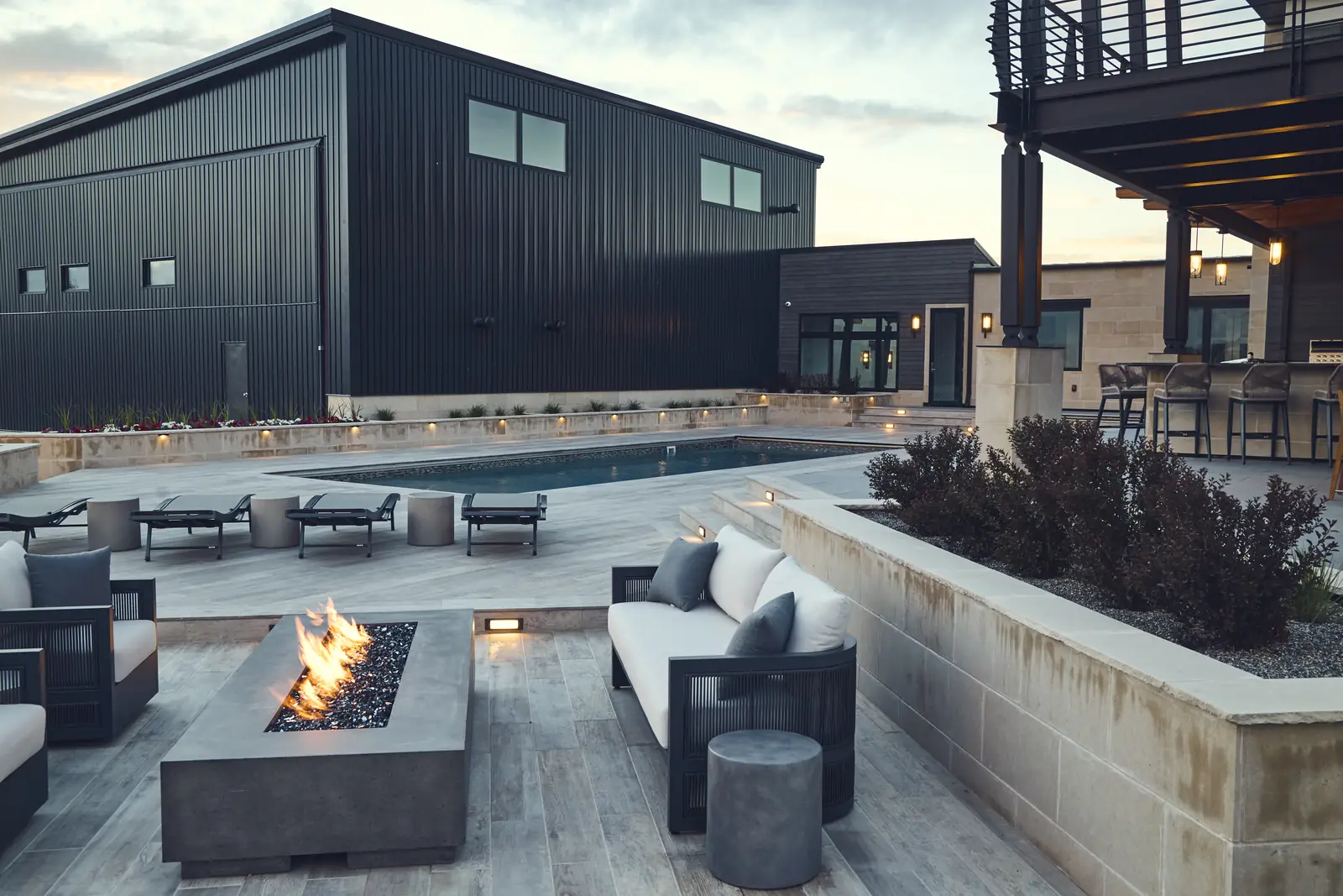 Burning concrete fire pit with outdoor sofas and limestone wall at dusk, Colorado