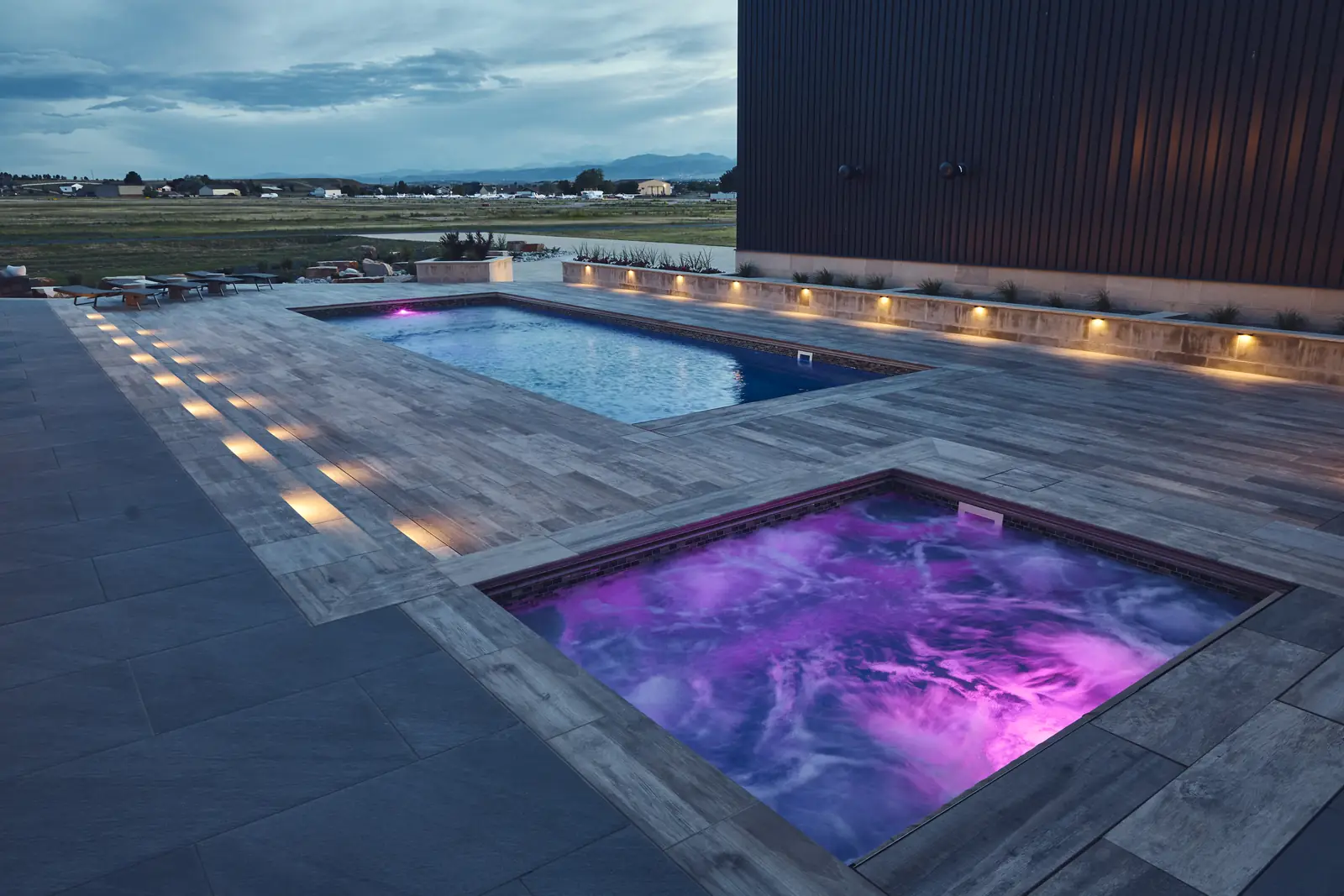 Elevated night view of a pool and purple-lit spa with deck lighting, Colorado